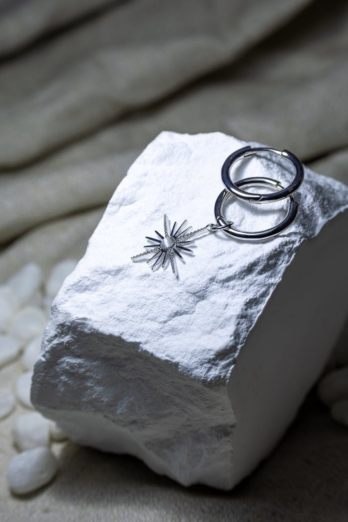 Stylish silver hoop earrings with a star pendant elegantly placed on a white stone surface.